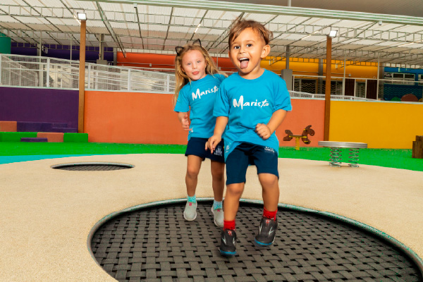 Duas meninas pequenas sentadas rindo uma para outra com o uniforme azul claro do Colégio Marista. 