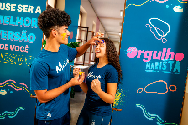 Duas meninas andando abraçadas e sorrindo, ao fundo outras duas andando lado a lado e sorrindo no ambiente escolar. 